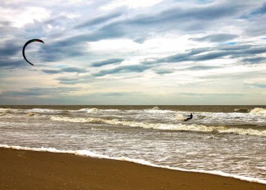 Bulutlu ve havadar bir günde uçurtma sörfü yapan bir adam