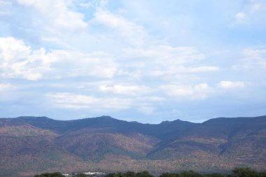 Jarilla yakınlarındaki dağların geniş manzara manzarası orman yangınından yanmış kahverengi toprağı gösteriyor. Küçük beyaz bir köy, büyük mavi gökyüzünün altında, beyaz bulutlu bir üste oturur.