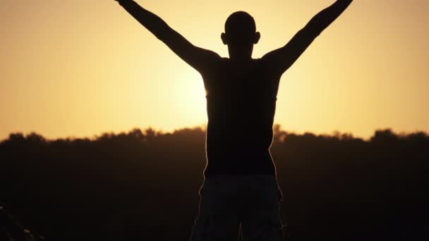 Silhouette of Young Man against Sunset Raising Hands Sides and Up (en inglés). Moción lenta — Vídeo de stock