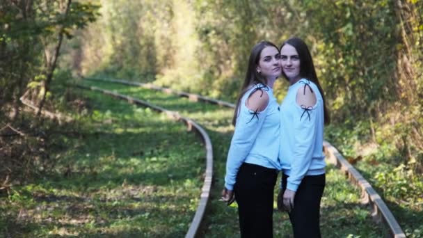 Des jeunes jumelles souriantes debout ensemble sur le chemin de fer. Regardez la caméra extérieure. — Video