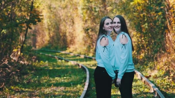 Sorrindo jovens gêmeas mulheres de pé juntos na estrada de ferro. Olhe para a câmera ao ar livre. — Vídeo de Stock
