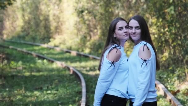 Des jeunes jumelles souriantes debout ensemble sur le chemin de fer. Regardez la caméra extérieure. — Video