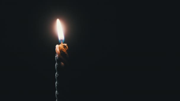 Una sola vela está encendida sobre un fondo negro. Llama de vela en la oscuridad. — Vídeos de Stock