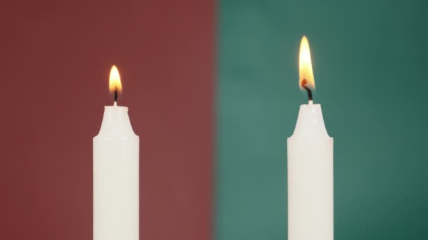 Dos velas se están quemando en un fondo rojo y verde cerca. — Vídeo de stock