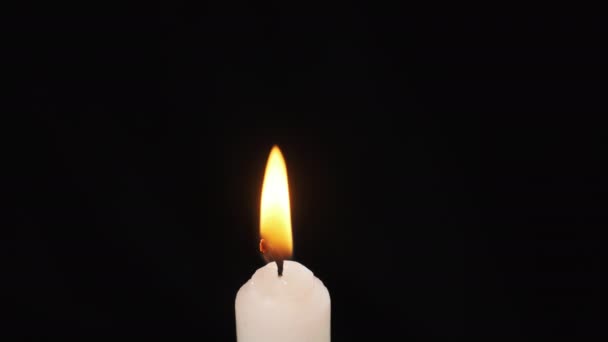 Uma única vela é lit em um fundo preto. Iluminação. Chama da vela — Vídeo de Stock
