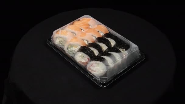 Los rollos de sushi giran en un contenedor de plástico sobre un fondo negro. Entrega de comidas — Vídeos de Stock