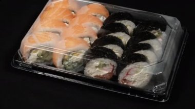 Suşi Rolls Royce, Siyah Arkaplan 'da plastik bir konteynırda dönüyor. Yemek teslimatı