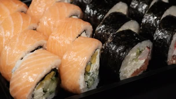 Sushi Rolls draait in een plastic container op een zwarte achtergrond. Maaltijden — Stockvideo
