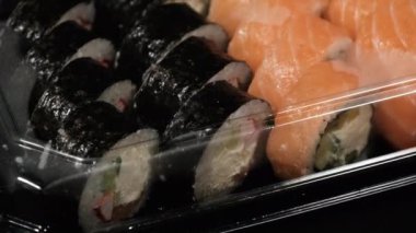 Suşi Rolls Royce, Siyah Arkaplan 'da plastik bir konteynırda dönüyor. Yemek teslimatı