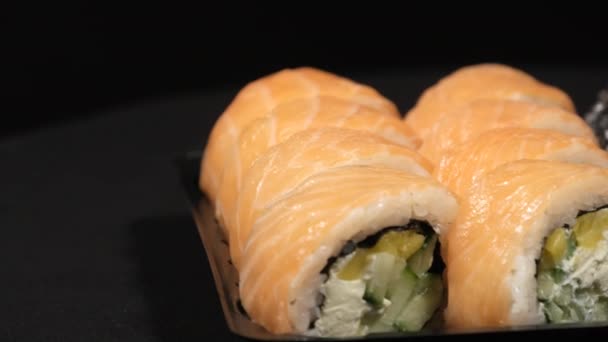 Sushi Rolls Περιστρέφεται σε ένα πλαστικό δοχείο σε μαύρο φόντο. Παράδοση γεύματος — Αρχείο Βίντεο