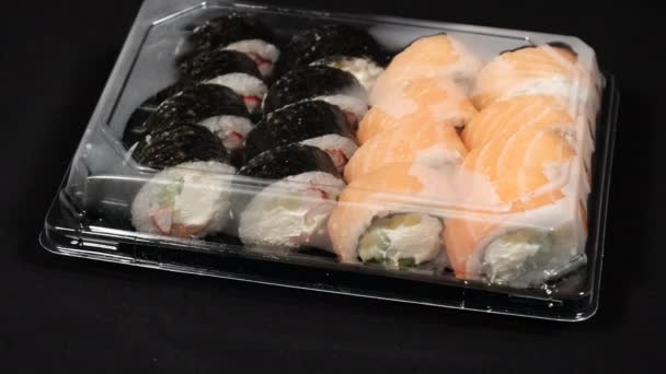 Sushi Rolls Obraca się w plastikowym pojemniku na czarnym tle. Dostawa posiłków — Wideo stockowe