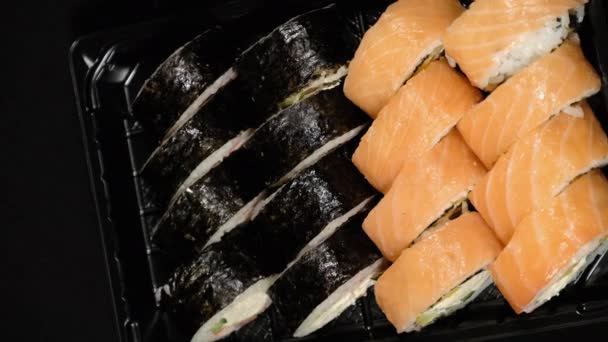 Vertikales Video. Sushi-Rollen rotieren in einem Plastikbehälter auf schwarzem Hintergrund — Stockvideo