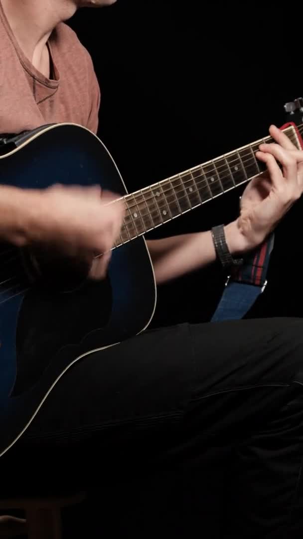 Vídeo vertical. Young Man Blogger toca una guitarra acústica sobre un fondo negro — Vídeos de Stock