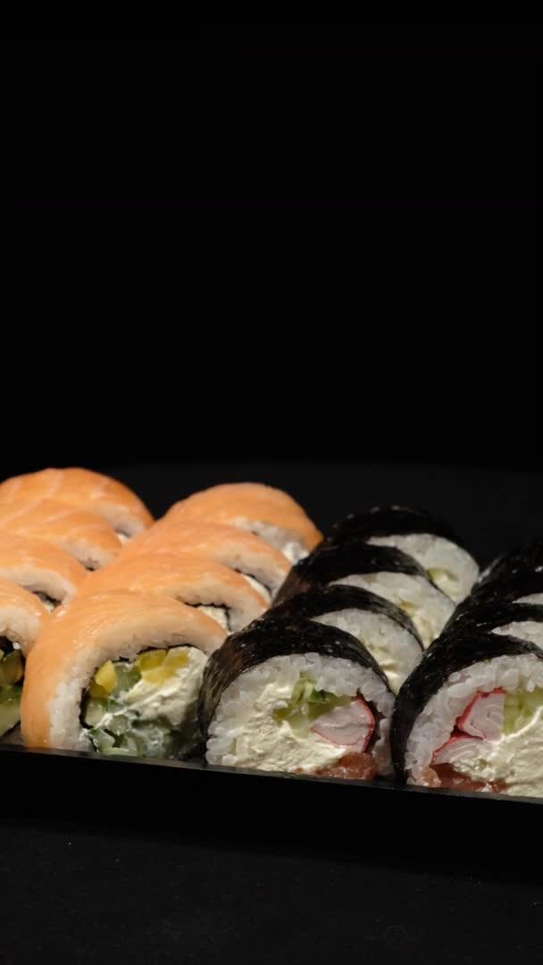 Vidéo verticale. Rouleaux Sushi tourne dans un récipient en plastique sur un fond noir — Video