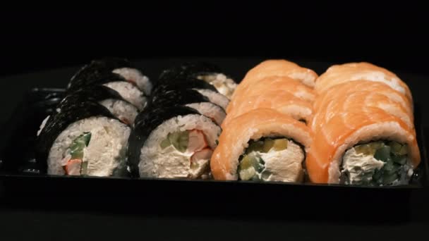 Los rollos de sushi giran en un contenedor de plástico sobre un fondo negro. Entrega de comidas — Vídeos de Stock