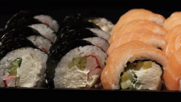 Sushi Rolls gira em um recipiente de plástico em um fundo preto. Entrega de refeições — Vídeo de Stock