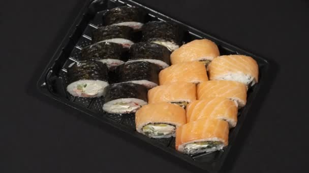 Rouleaux de sushi tourne dans un récipient en plastique sur un fond noir. Livraison de repas — Video