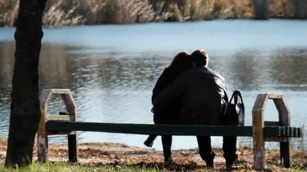 Giovane coppia romantica seduta su una panchina in un parco autunnale vicino al fiume. Caduta. — Video Stock