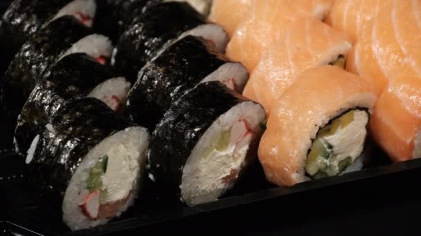 Sushi Rolls gira em um recipiente de plástico em um fundo preto. Entrega de refeições — Vídeo de Stock