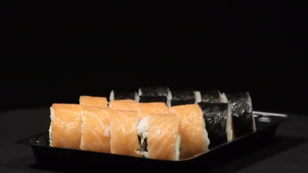 Sushi Rolls roterar i en plastbehållare med svart bakgrund. Måltidsleverans — Stockvideo