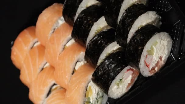 Vidéo verticale. Rouleaux Sushi tourne dans un récipient en plastique sur un fond noir — Video