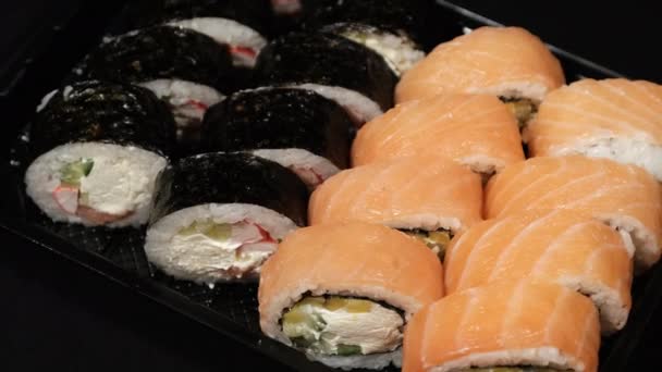 Sushi Rolls gira em um recipiente de plástico em um fundo preto. Entrega de refeições — Vídeo de Stock