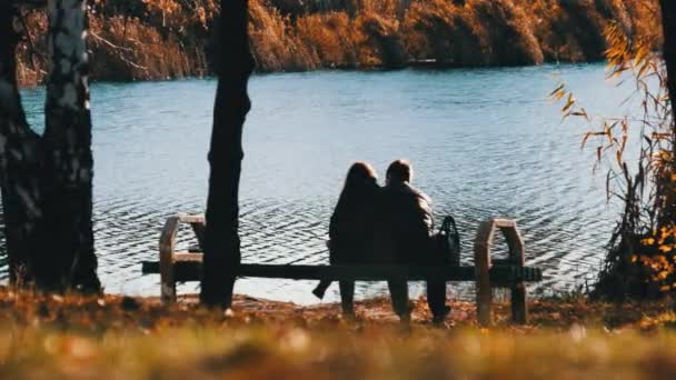 Jong romantisch stel zittend op een bank in een herfstpark aan de rivier. Vallen.. — Stockvideo