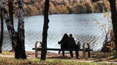 Genç Romantik Çift Nehir kenarındaki bir sonbahar parkında bir bankta oturuyor. Düş.