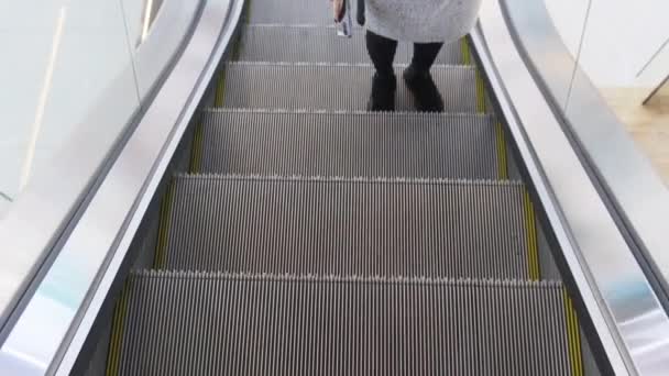 Vista de las piernas de una mujer que asciende una escalera mecánica vacía en un centro comercial. Centro comercial. — Vídeo de stock
