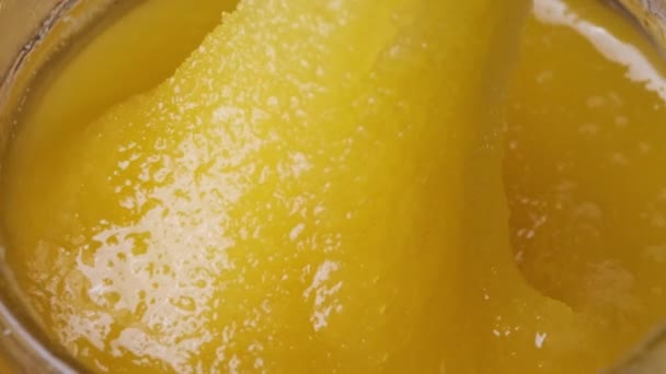 水晶蜂蜜在一个罐子里。特写镜头。勺子泡在厚厚的蜂蜜里 — 图库视频影像