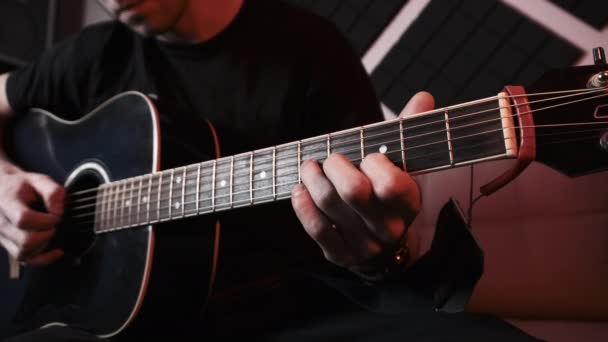 Jongeman speelt akoestische gitaar tijdens het zitten op de bank in Home Recording Studio — Stockvideo