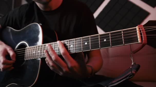 Jovem tocando guitarra acústica enquanto sentado no sofá em estúdio de gravação em casa — Vídeo de Stock