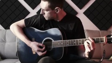 Evde Kayıt Stüdyosunda Kanepede otururken Akustik Gitar Çalan Genç Adam
