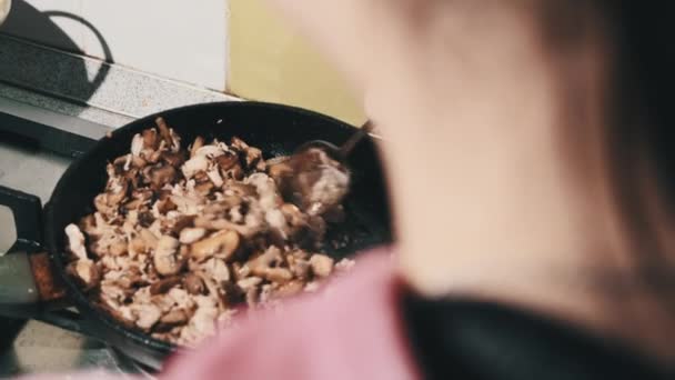 Молодая женщина готовит жареные грибы с сыром и мясом на домашней кухне — стоковое видео
