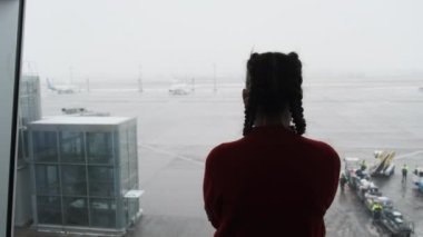 Havaalanında maskeli genç bir kadın gezginin silüeti uçaklara bakıyor.