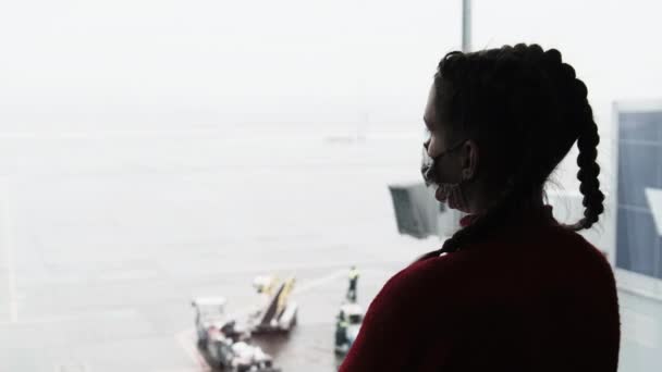 Silhouette of a Masked Young Woman at Airport Terminal Window Looking at Planes — стокове відео