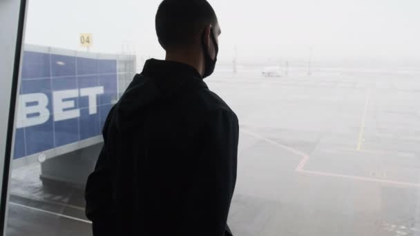 Silhouette eines maskierten jungen Mannes am Terminal des Flughafens beim Blick auf Flugzeuge — Stockvideo