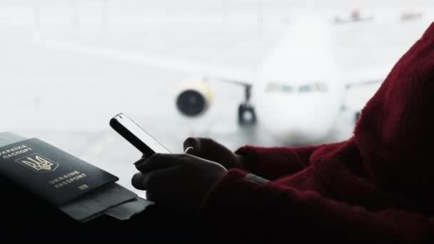Jovem mulher no aeroporto sala de espera senta-se e usando um smartphone pela janela — Vídeo de Stock