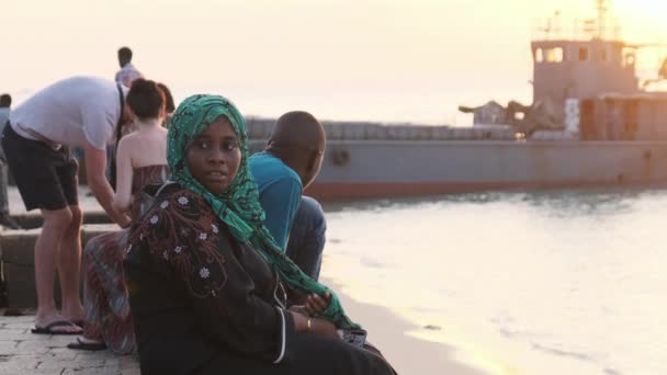 Afrikansk muslimsk kvinna i hijab sitter på strandpromenaden nära Ocean för att titta på solnedgången — Stockvideo