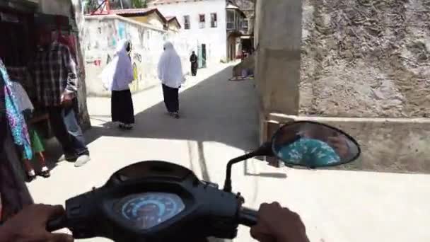 Езда на скутере по узким грязным улицам каменного города с бедными африканцами — стоковое видео