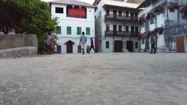 Grupp av afrikanska pojkar spelar fotboll mitt i ruinerna av smutsiga Stone Town, Zanzibar — Stockvideo