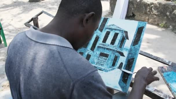 Un artista di strada dipinge un quadro con pitture ad olio nel parco su una panchina in Africa. — Video Stock