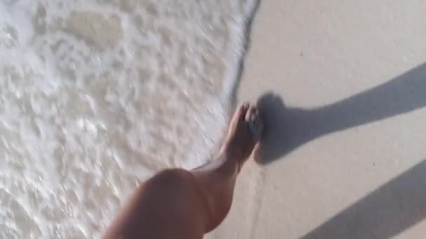 Punto de vista de las piernas de una mujer joven caminando por la arena blanca y olas de surf de la orilla del mar — Vídeos de Stock