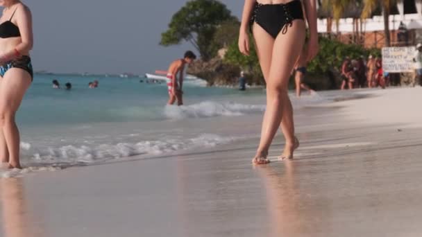 Piernas de una mujer joven caminando por la arena blanca y olas de surf de la orilla del mar — Vídeo de stock
