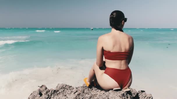 Kızıl Bikini 'deki Genç Kadın Taş Resifi' nde oturuyor ve Okyanus 'a bakıyor. — Stok video
