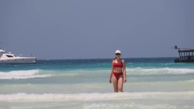 Kırmızı mayo giymiş genç bir kadın Cennet Sahili 'ndeki Turkuaz Okyanusu' na yürür.