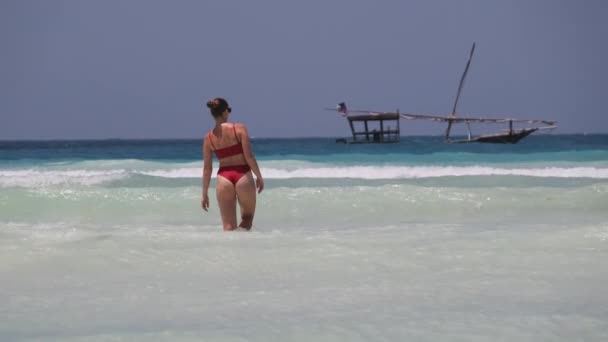 Mladá žena v červených plavkách vejde do tyrkysového oceánu na pláži v ráji