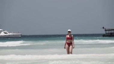 Kırmızı mayo giymiş genç bir kadın Cennet Sahili 'ndeki Turkuaz Okyanusu' na yürür.