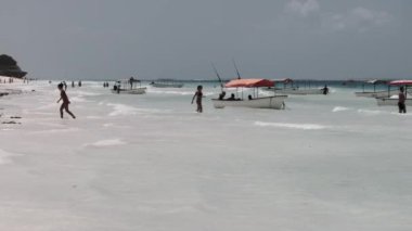 İnsanlar, demirli zevk teknelerinin yanındaki kumlu kumsalda dinleniyorlar, Zanzibar.