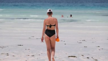 Siyah mayo giymiş genç bir kadın Cennet Sahili 'ndeki Turkuaz Okyanusu' na giriyor.